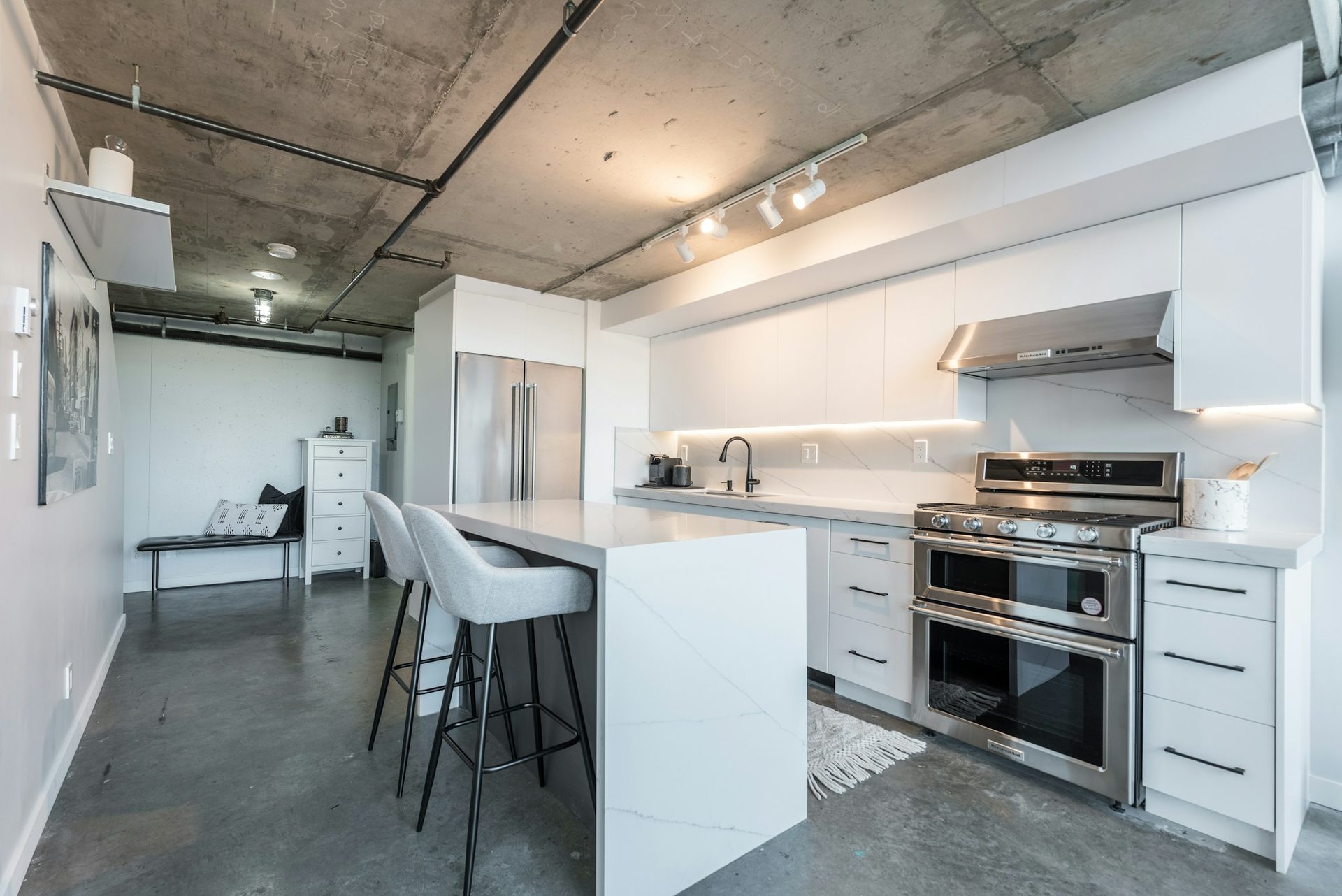 Kitchen with a concrete ceiling, white island and bar stools